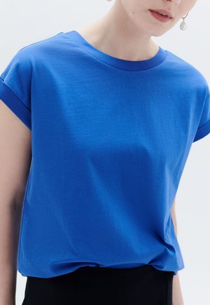 T-shirt blu a maniche corte realizzato in morbido cotone. Presenta un collo arrotondato e una vestibilità rilassata, con le maniche arrotolate e una texture liscia.