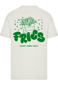 T-shirt bianco con una grafica verde di un contenitore di patatine, messo in risalto da un testo in grassetto che recita "PATATINE" e la frase "SOLO VIBRE CROCCANTI."