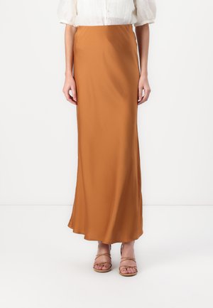 Jupe longue et fluide dans une teinte orange-brun chaude ; fabriquée en tissu léger avec une texture lisse ; associée à des sandales à lanières.