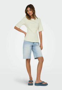 Haut court jaune clair associé à un short en jean bleu clair. Le short a un ourlet effiloché, complété par des sandales bleues à enfiler.
