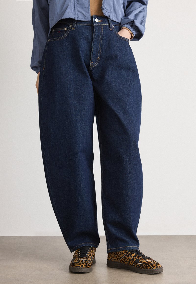 Jeans de mezclilla azul oscuro de cintura alta con un ajuste relajado, diseño de cinco bolsillos y detalles de costura visibles. Combinados con zapatos de estampado de leopardo.
