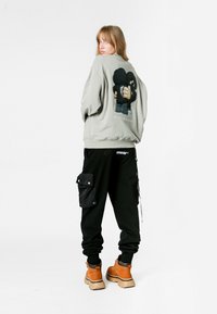 Sudadera gris con un gráfico de dibujos animados en la parte posterior, combinada con joggers negros que tienen bolsillos tipo cargo. El modelo lleva botas beige.