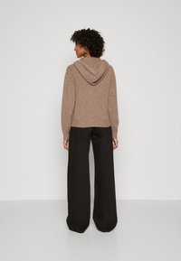 Felpa a maglia marrone con una texture morbida e cappuccio, abbinata a pantaloni neri larghi. La vestibilità è rilassata e informale, con polsini a coste.