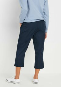 Marineblauwe cropped broek van katoen, met omgeslagen mouwen, twee achterzakken en een relaxed fit. Gecombineerd met een lichtblauw topje en sneakers.