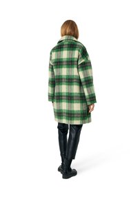 Green and cream plaid oversized coat made of wool blend, featuring large lapels, long sleeves, and a straight cut. Worn over black leather pants.