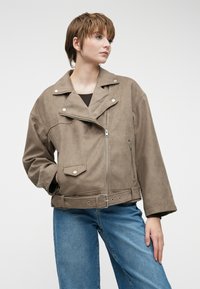 Brun semsket bikerjakke med en cropped design, dobbel klaff, trykknapper, frontglidelås og sidelommer, kombinert med blå jeans.