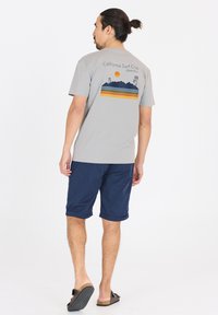 Harmaa lyhythihainen T-paita, jossa on Kalifornian surf-klubin grafiikka. Suunnittelussa on vuoria, aurinko ja raidallisia yksityiskohtia tummansinisessä, oranssissa ja vihreässä.