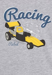 T-shirt cinza com um gráfico de um carro de corrida amarelo com chassi preto, pneus detalhados e marcas de velocímetro. O texto diz "Rebelde das Corridas".