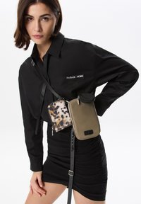 Maglietta nera con etichetta "Profonde - NOIRE", accessoriata con due borse: una a fantasia marrone e beige, l'altra verde oliva con cerniera.