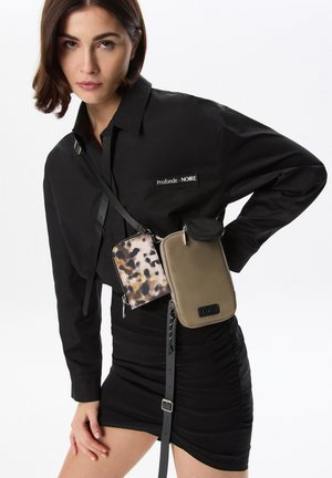 Schwarzes Shirt mit dem Etikett "Profonde - NOIRE", accessoriert mit zwei Handtaschen: eine gemustert in Braun und Beige, die andere olivgrün mit einem Reißverschluss.