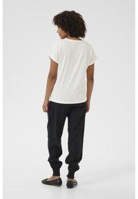 T-shirt en coton écru, avec des manches roulées. Assorti à un pantalon de jogging noir, resserré au niveau des chevilles, porté avec des chaussures plates.