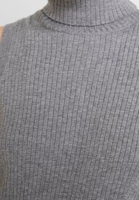 Grå ribbad, stickad ärmlös polotröja med en tight passform och subtil textur, som har en hög krage och jämna vertikala ränder.