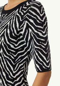 Zwart-wit trui met zebra-print, korte mouwen en een ronde hals. De stof lijkt zacht met een gestructureerde afwerking.
