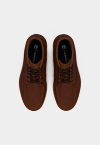 Καφέ δερμάτινα παπούτσια με υφή, στρογγυλή μύτη και μαύρα κορδόνια. Διαθέτουν τακούνι από καφέ καουτσούκ και σήμανση στο εσωτερικό.