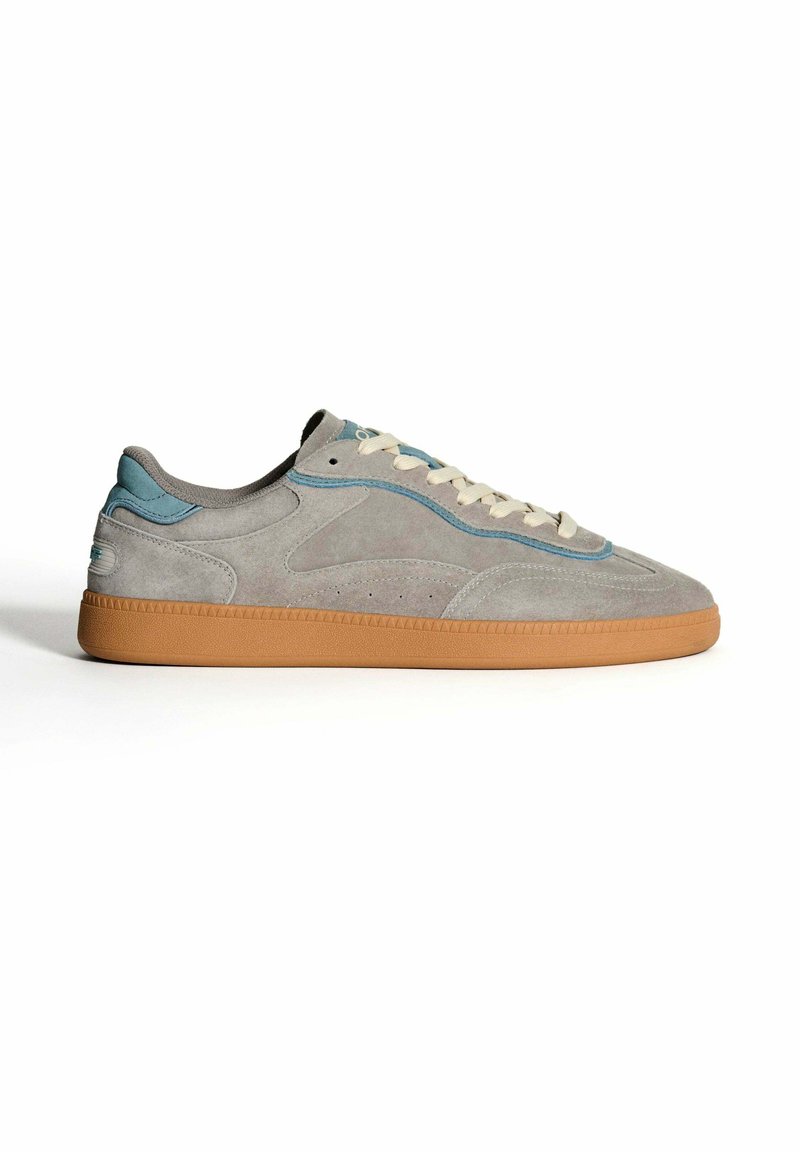 Sneaker in suede grigia con dettagli blu, lacci bianchi e suola in gomma naturale, mostrata di lato su uno sfondo bianco.