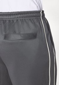 Dark gray athletic pants with a smooth texture, featuring a drawstring waistband and contrasting white side stripes. Includes a back pocket.