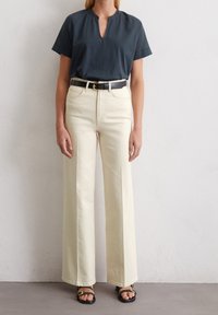 Mörkgrå kortärmad topp med nyckelhålsutskärning, kombinerad med högmidjade off-white vida byxor och svarta sandaler med guld detaljer.