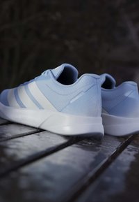 Zapatillas deportivas azul claro con tela texturizada, rayas blancas y una suela suave y ligera. Presentan un patrón geométrico en el talón.