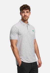 Vaaleanharmaa pikeepaita, valmistettu sileästä kankaasta, jossa on klassinen kaulus, lyhyet hihat ja vihreä logo vasemmassa rinnassa.