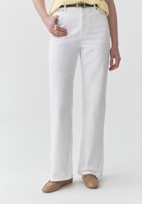 Jeans bianchi a gamba larga in cotone, con vita alta, passanti per cintura e tasche anteriori. Abbinate a scarpe slip-on color beige e a una maglietta gialla.
