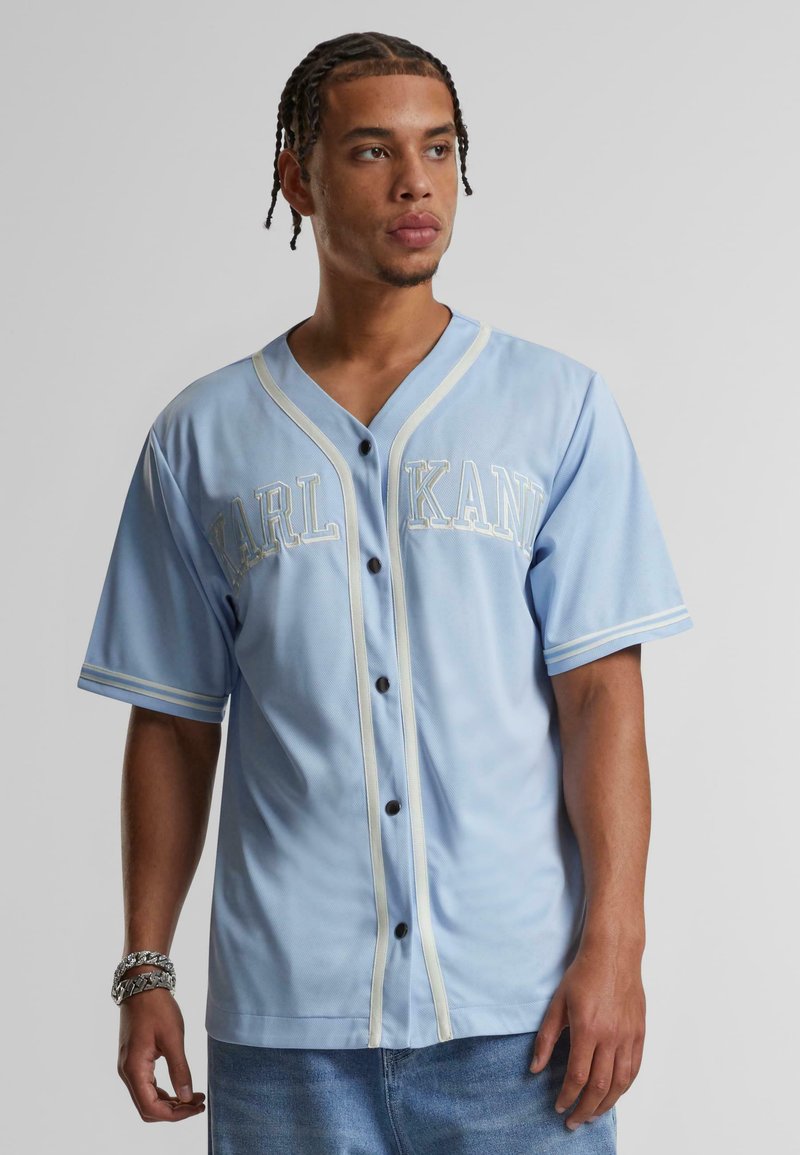 Maglietta da baseball blu chiaro con rifiniture bianche ed il logo ricamato "KARL KANI". Presenta bottoni, maniche corte e una vestibilità comoda.
