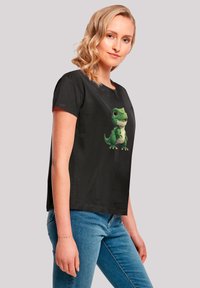 Black T-shirt featuring a green cartoon dinosaur graphic, short sleeves, relaxed fit, and cotton material. Casual style with a playful design.