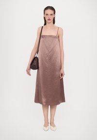 Satin, mid-length kjole i mauve med tynne spaghettistropper; har en avslappet passform og glatt tekstur. Kombinert med en liten brun veske og lyse hæler.