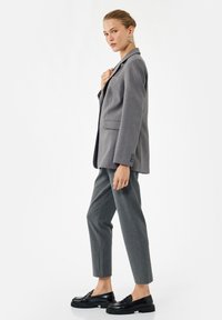 Gray wool blazer with notched lapels, two front pockets, paired with tailored gray pants and black loafers, featuring chunky soles.