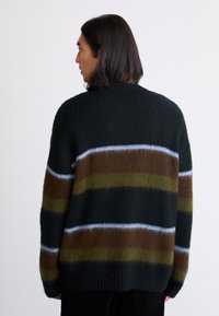 Oversized strikket sweater i mørkegrøn med brune, oliven- og lyseblå striber. Har en blød tekstur og ribbede manchetter.