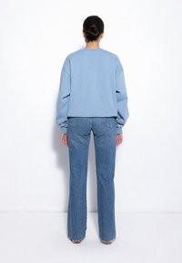 Jasnoniebieski, oversize'owy sweatshirt z opuszczonymi ramionami, połączony z wysokim stanem, lekko rozszerzającymi się niebieskimi dżinsami z postrzępionymi detalami na dole.