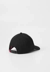 Casquette noire à forme arrondie, fabriquée en tissu, dotée d'une visière courbée, d'une fermeture ajustable à pression et de trous de ventilation sur le dessus.