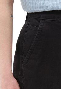 Pantalones de algodón negros con bolsillos laterales, que presentan una cinturilla plana y una textura sutil. Vista en primer plano que resalta los detalles de la costura.