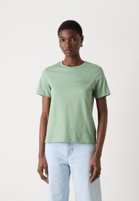 T-shirt in cotone verde menta con maniche corte, scollatura rotonda e un discreto logo ricamato sul petto. Vestibilità casual con texture morbida.