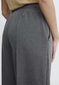 Sive teksturirane hlače z elastičnim pasom in stranskimi žepi, ki prikazujejo natančno prileganje. Poudarjen pogled na zadnjo stran.
