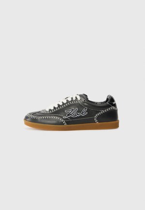 Sneaker in pelle nera con cuciture e lacci bianchi, dotata di una suola in gomma marrone e logo ricamato "Karl" sul lato.