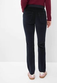 Navy stretchbroek met een gladde textuur, uitgerust met twee achterzakken en een elastische tailleband, gecombineerd met lichtroze casual schoenen.
