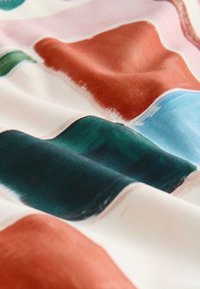 Tissu doux avec des blocs abstraits de couleurs orange brûlé, sarcelle, bleu et vert sur un fond blanc avec une texture lisse.