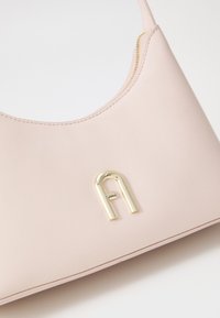 Sac à main en cuir rose avec une texture lisse, présentant un logo en métal doré bien en vue et une fermeture éclair le long du bord supérieur.