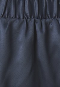 Țesătură de satin bleumarin, cu o textură netedă, prezentând detalii plisate pentru un plus de dimensiune și finețe.