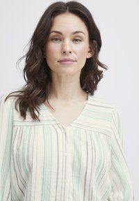 Camicia con abbottonatura in tessuto leggero con righe verticali in verde menta, beige e lavanda. Presenta un colletto a V e maniche lunghe.