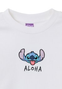 Weißes Baumwollhemd mit geripptem Ausschnitt, versehen mit blauem besticktem Cartoon-Charakter und dem Text "ALOHA" darunter.