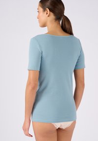 Top azzurro chiaro a maniche corte con scollatura rotonda, design aderente e texture morbida. Vista dal retro che mostra il tessuto liscio e le cuciture.