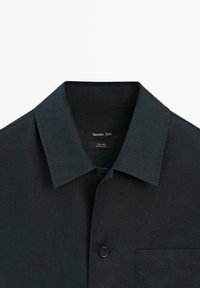 Chemise noire en lin à boutons, col classique et poche poitrine, étiquetée Massimo Dutti, fabriquée en Chine.