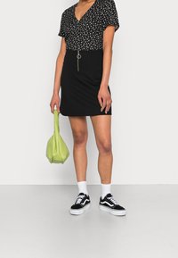Haut à imprimé floral noir avec manches courtes, associé à une jupe noire avec poches frontales, stylé avec des chaussettes blanches et des baskets noires. Sac vert.