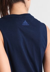 Sininen ilman hihoja urheilu paita, joka on valmistettu sileästä kankaasta. Selkäkauluksessa on pieni, tumma sininen Adidas-logo.