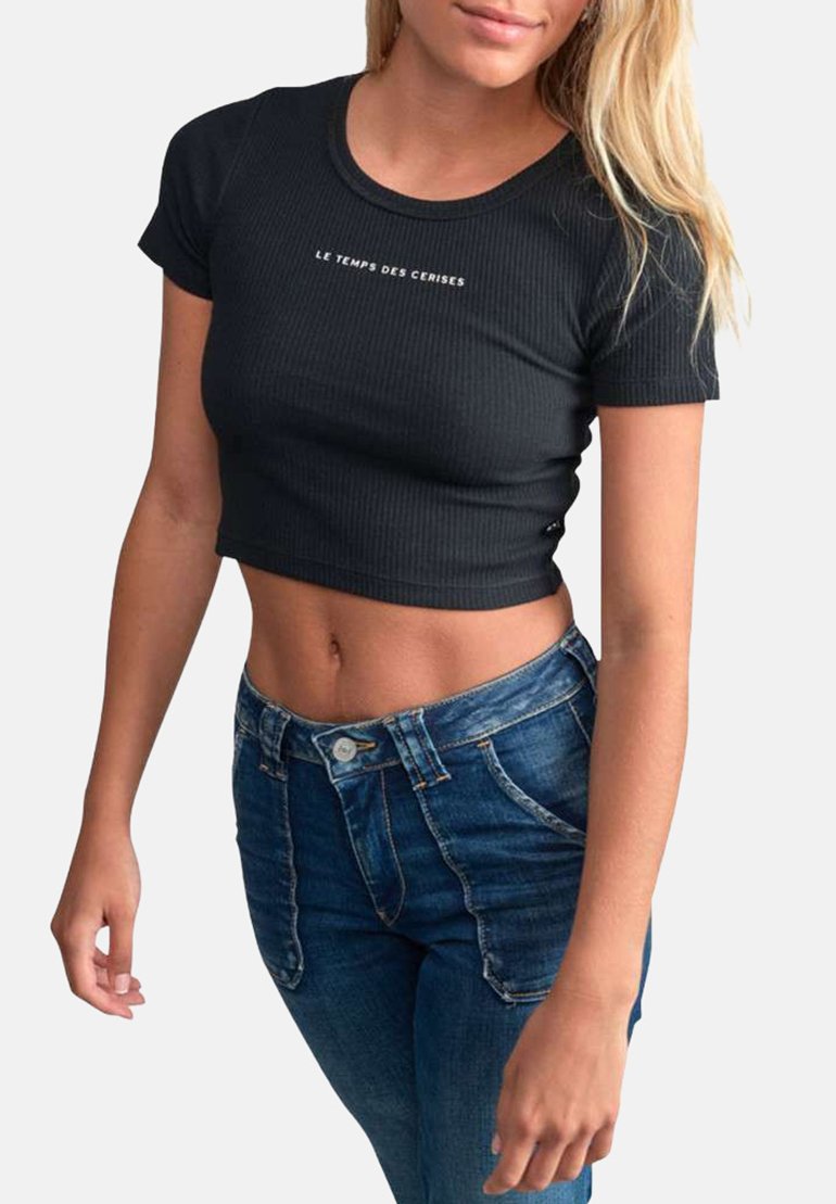 Crop top noir côtelé avec des manches courtes et le texte blanc "LE TEMPS DES CERISES" sur le devant, associé à un jean bleu taille haute.