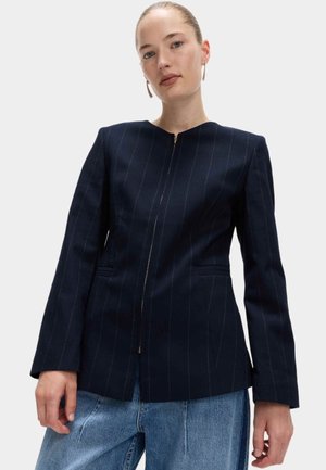 Námořnický proužkovaný blazer s elegantním střihem, s zipovým uzávěrem a předními kapsami, doplněný světle modrými širokými džíny.