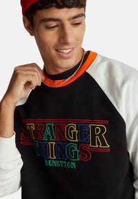 Czarna bluza z kolorowym haftem "STRANGER THINGS", pomarańczowym kołnierzem i białymi rękawami. Posiada luźny krój i strukturę tkaniny.
