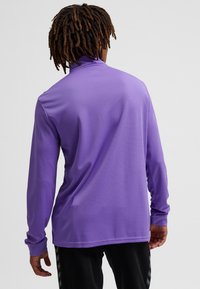 Lila Langarmshirt mit strukturiertem Finish und hohem Kragen, mit taillierten Ärmeln und einem dezenten Design auf der Rückseite.