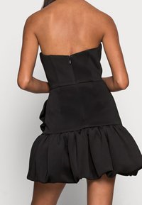 Zwarte strapless jurk met een getailleerd lijfje en een geruffelde zoom. Heeft een achterritssluiting en een gladde stoftextuur.